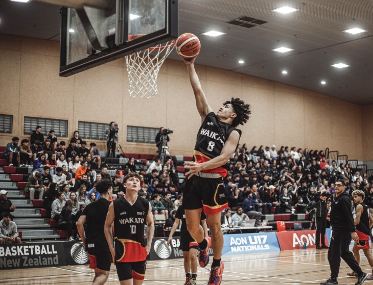 A young male basketball player jumps up to get the ball in the hoop. 