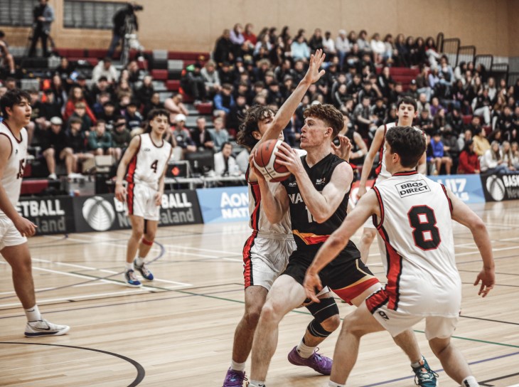 A young male basketball player tries to push his way past two opponents. 