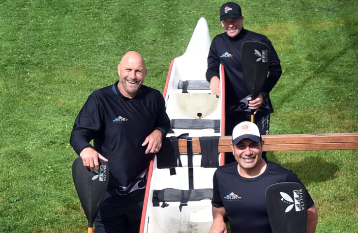 Brendon Timmins with two other crew members standing next to a waka ama boat.