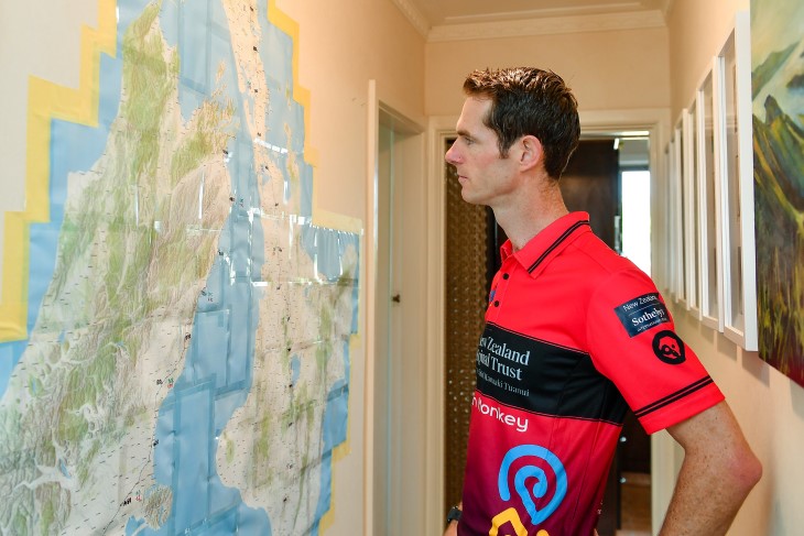 Brendon Vercoe standing in his house looking at a map of New Zealand on the wall.