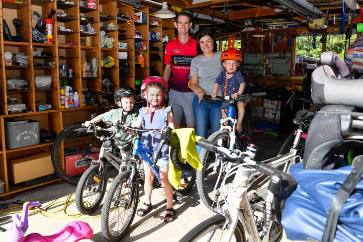 Brendon Vercoe in his garage with his wife and three young children, who are all sitting on bikes. 
