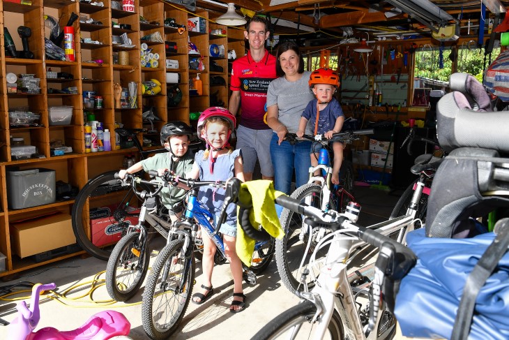 Brendon Vercoe in his garage with his wife and three young children, who are all sitting on bikes.