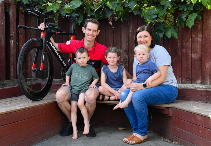 Brendon Vercoe sitting down with his family and holding his bike. 