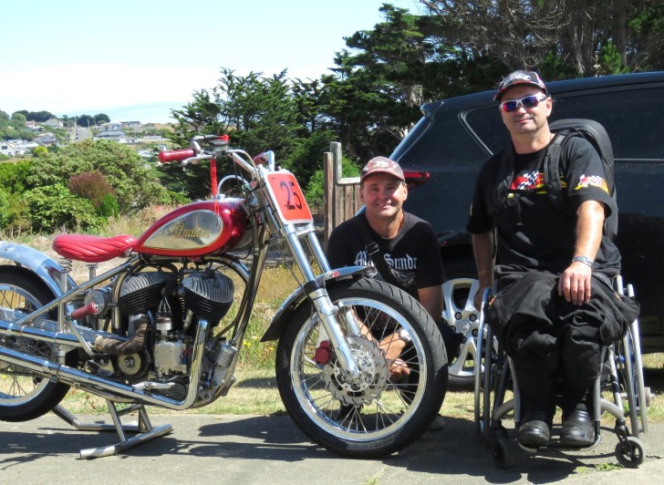 Brett Ladbrook sitting in his wheelchair next to his friend and a motorbike.
