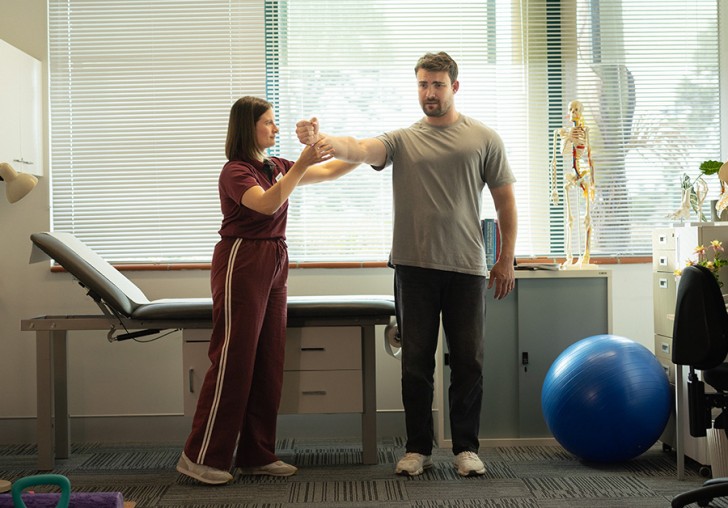 A man doing exercises on his arm with a female physio.