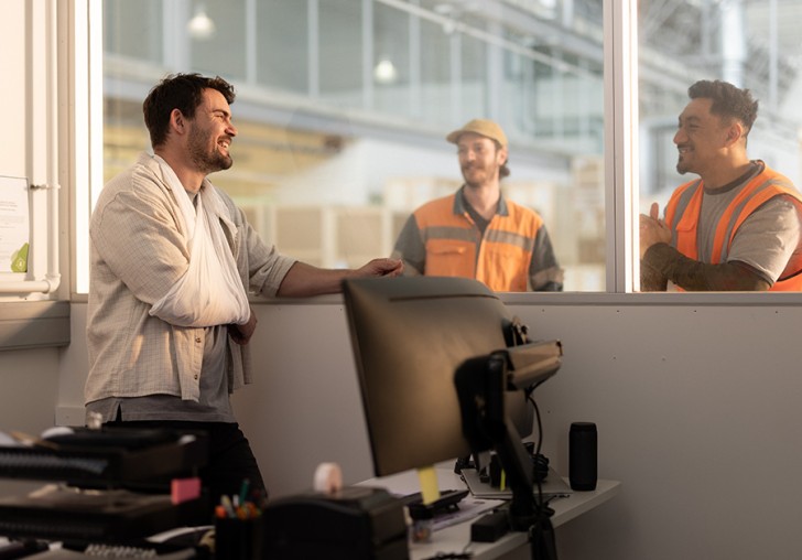 A man at work with his injured arm in a sling laughing with his colleagues.