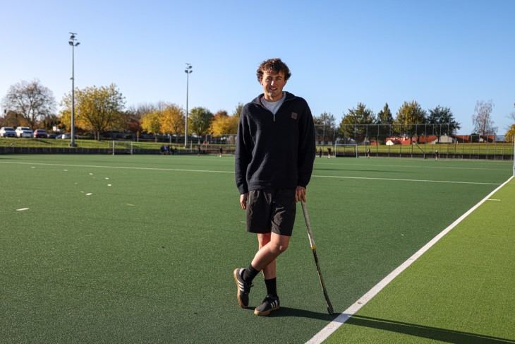 Campbell Gray standing on a hockey turf and leaning on his hockey stick. 