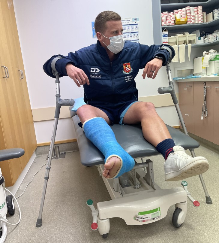 Carl Perry sitting in a medical centre with his leg in a cast and holding crutches. 