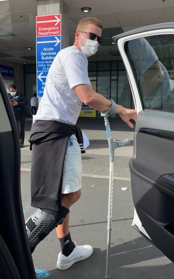 Carl Perry getting out of a car with crutches and his foot in a moon boot. 