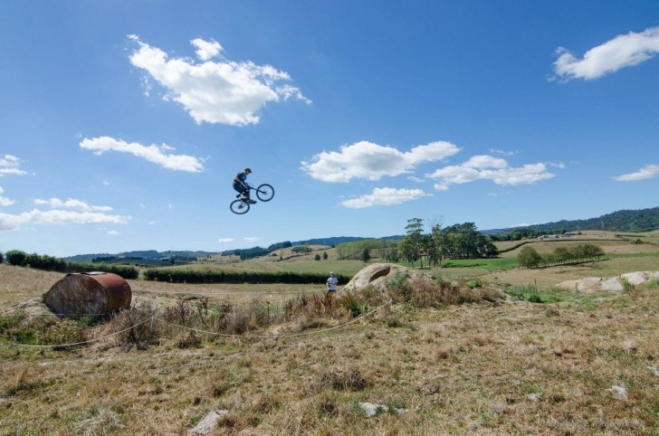 Clinton Williams in mid-air after riding over a ramp on a mountain bike trail.