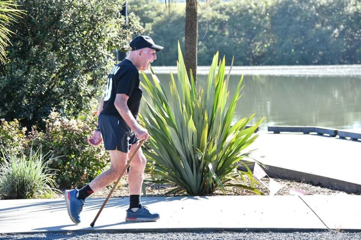100-year-old Colin Thorne walking on a path next to a lake. 