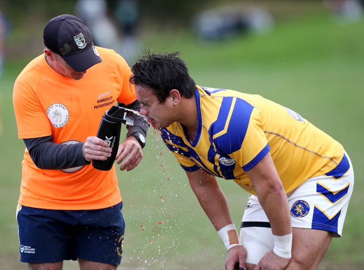 A physio using a water bottle to wash blood off the face of a rugby league player on the field.