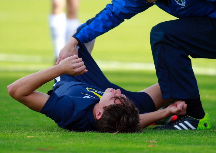 A football player lying on the ground with a physio bending down over him.