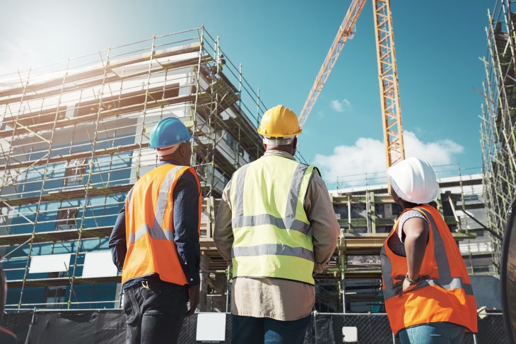 Three construction workers standing together and looking up at a building site. 