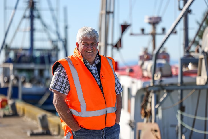 Doug Saunders-Loder, president of the NZ Federation of Commercial Fisherman, standing on a wharf in front of a boat.