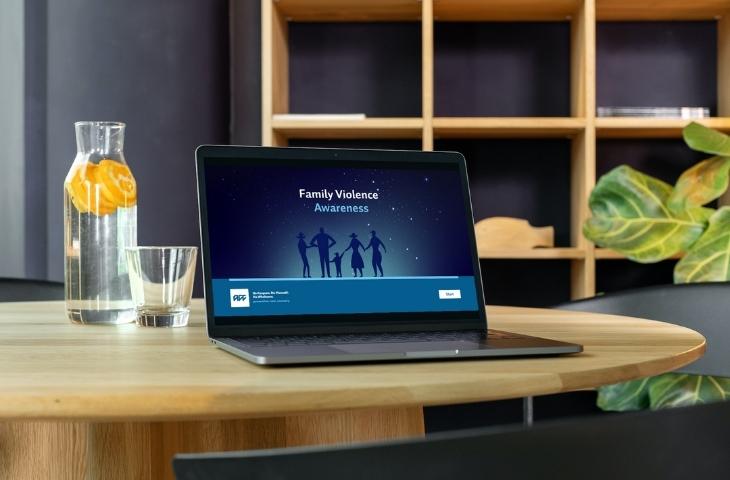 A photo showing a laptop sitting on a desk, on the screen is the home page of the ACC Family Violenc