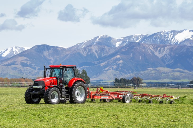 A farmer on a tractor ploughing a field with snow-capped mountains in the background.