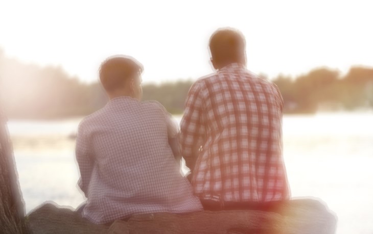 Father and son, sitting by a lake talking