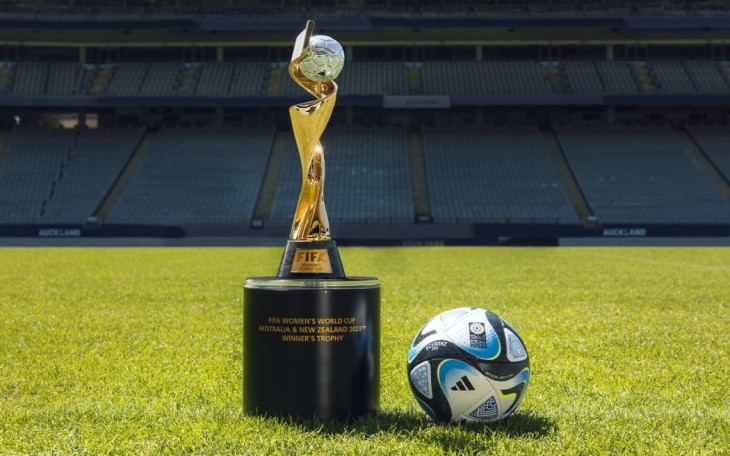 A photo of the FIFA Women's World Cup trophy and a football sitting on the pitch at a stadium.
