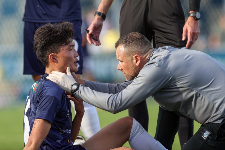 A football player sitting on the field being checked for concussion by a physio.