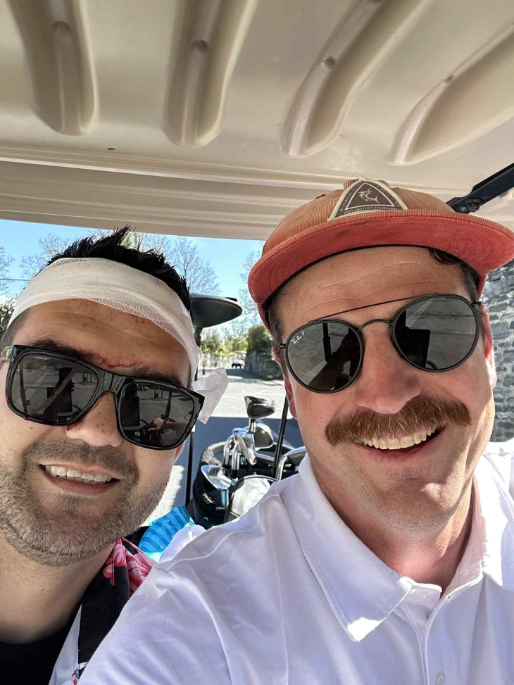 A selfie of Grant Sweeney and his friend in a golf cart showing a bandage around Grant's head,