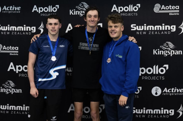 Guy Harrison stands with two other swimmers, they all have medals around their necks. 