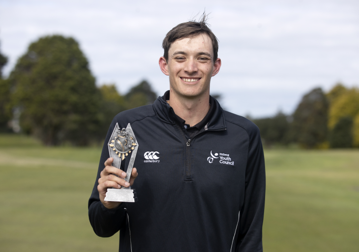 Guy Harrison standing on a golf course holding a trophy in his hand. 