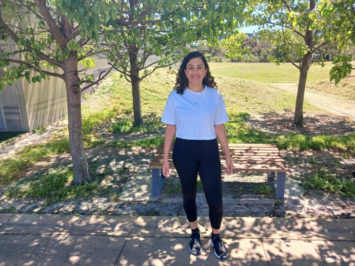 Hala standing on a path with trees and a park behind her.