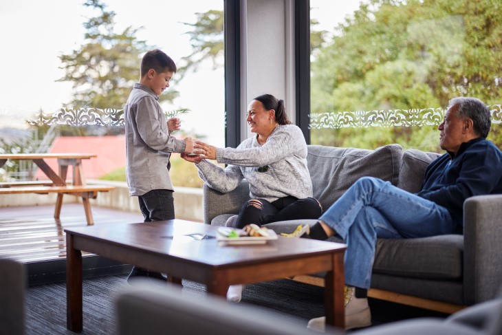 hapai image A boy giving a cup of coffee to a woman sitting on a couch as a man looks on.