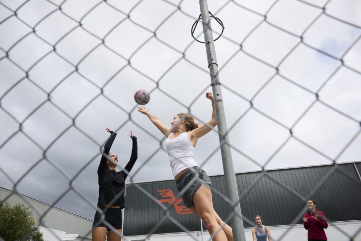 A female netball player shooting for goal while a goal defence player tries to block the shot.