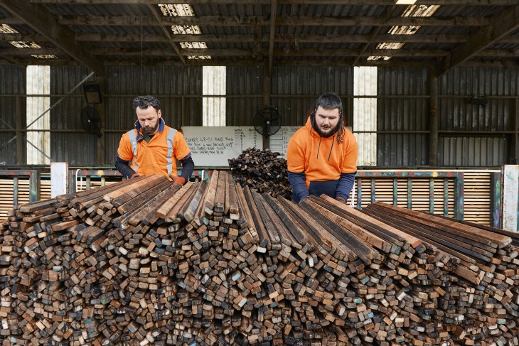 Two male workers loading planks into a pile in a lumbar yard.