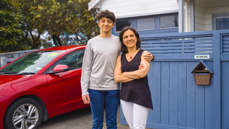 A young man standing with his mother next to a car outside their house.