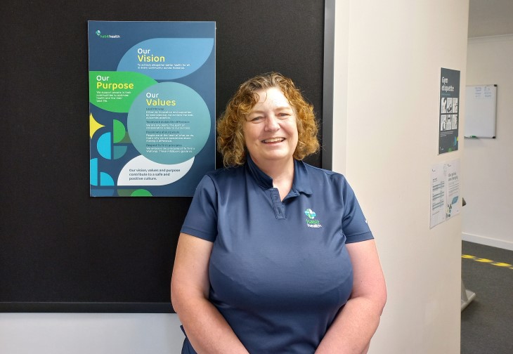 Jane Harding standing in the corridor of a medical centre and smiling. 