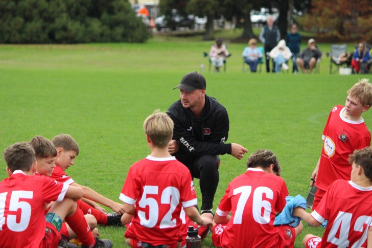 Jarrod Young kneeling on the pitch and talking to a young group of players.