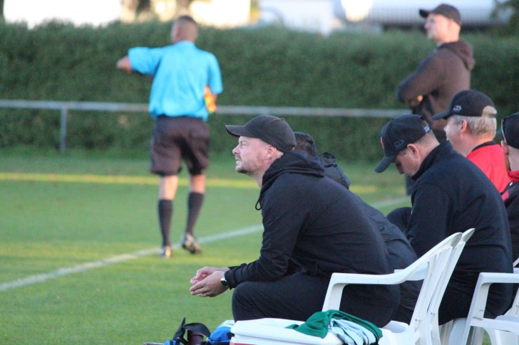 Jarrod Young sitting on the side of a football pitch coaching his team.