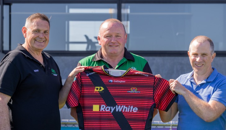 Nigel Walsh standing between two other men holding a South Canterbury rugby jersey.