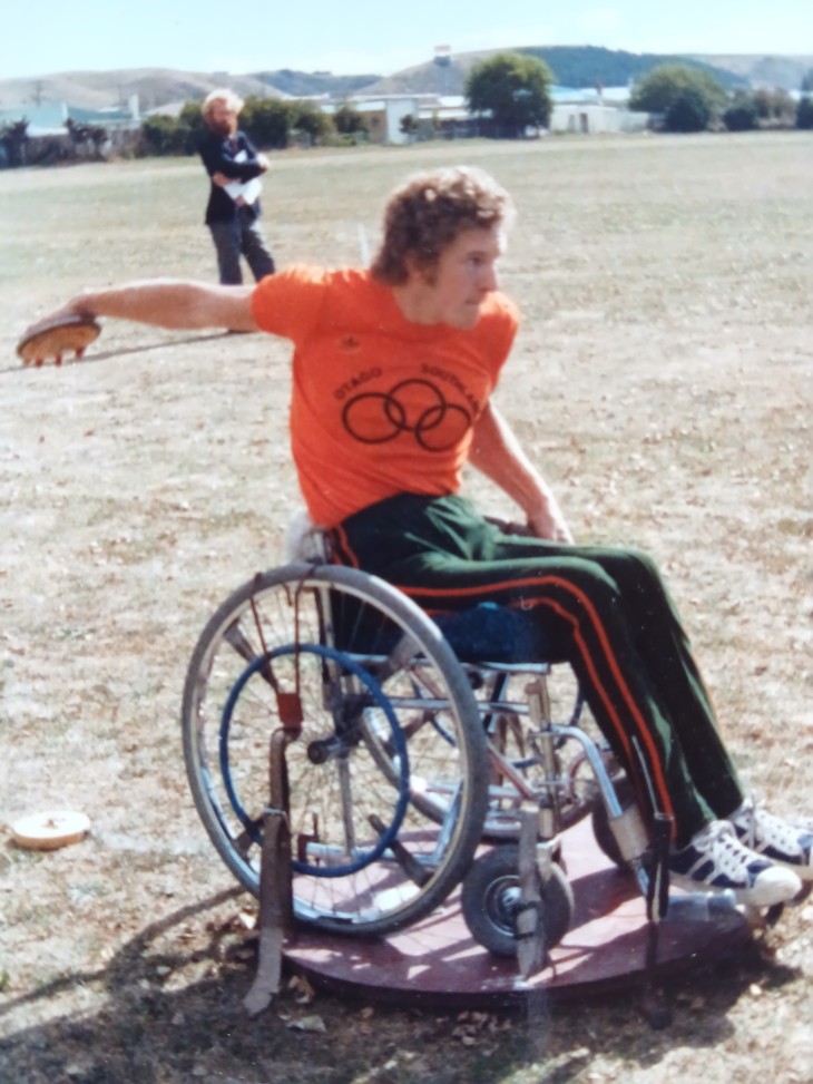 John Marrable sitting in a wheelchair throwing a discus in the 1970s.