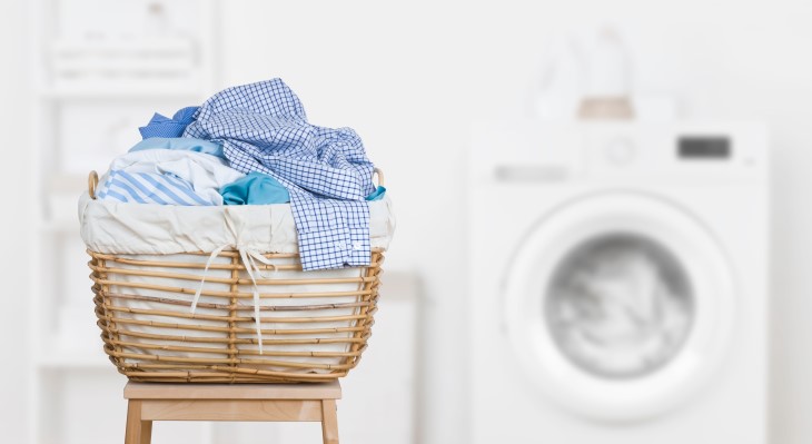 A basket of clothes on a table in front of a washing machine. 