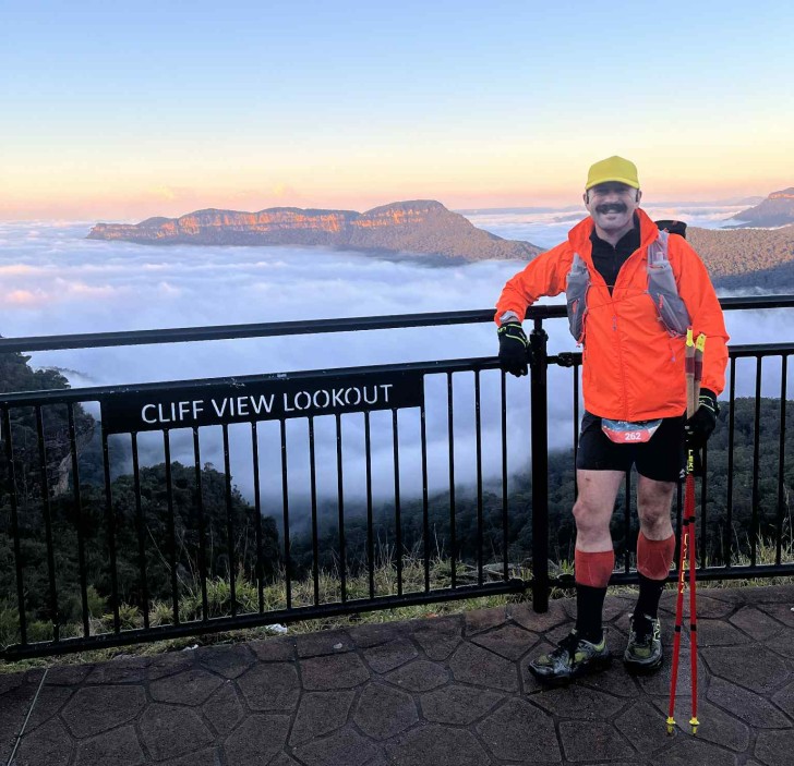 Mark Baker standing at a lookout with a mist-covered mountain behind him.