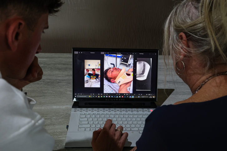 Matt Burchell and his mother shown from behind looking at photos from his accident and recovery on a laptop.