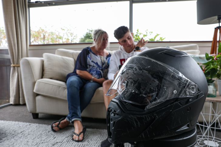 Matt Burchell and his mum sitting on a couch in their living room with his motorcycle helmet in the foreground.