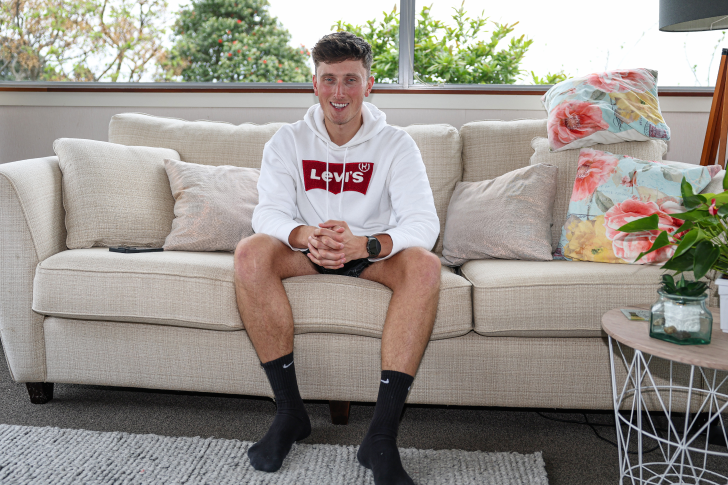 Matt Burchell sitting on the couch at home smiling at the camera.