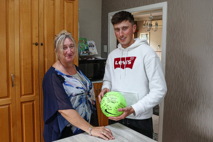 Matt Burchell with his mother holding a football signed with get-well messages by his friends.