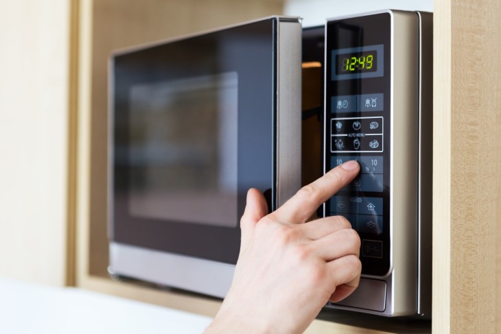 A human hand presses the buttons on a microwave. 