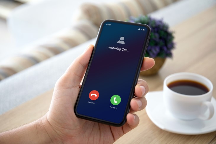 A man holds his mobile phone as it receives an incoming call. 