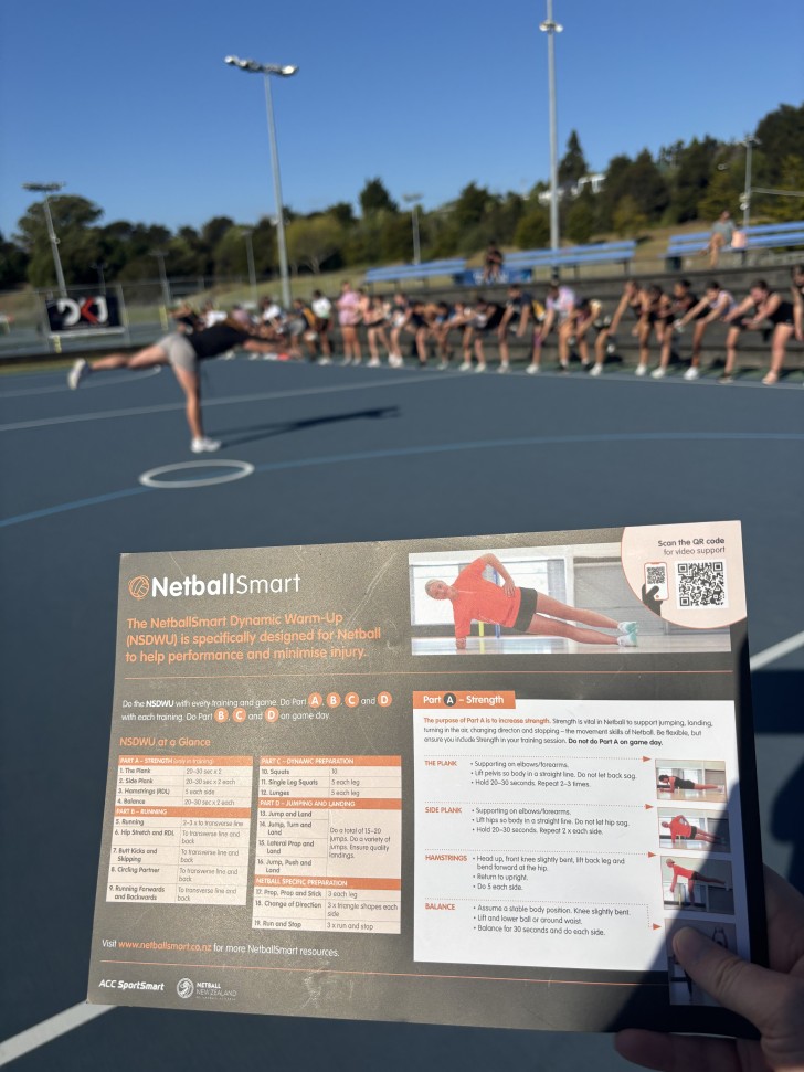 A close-up shot of a NetballSmart guide with a session taking place in the background on a netball court.