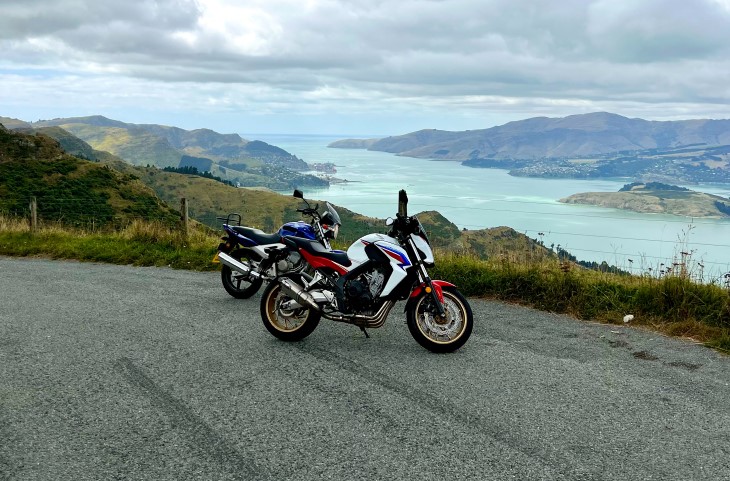 The motorbikes owned by Nick Grant and Sean Dickey standing at the top of a hill with a beautiful harbour setting in the background.