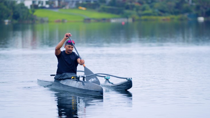 Peter Cowan paddling in his waka ama outrigger canoe on a lake. 