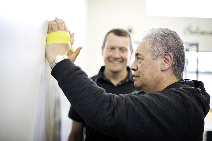 A man doing a rehabilitation exercise while his physio watches.