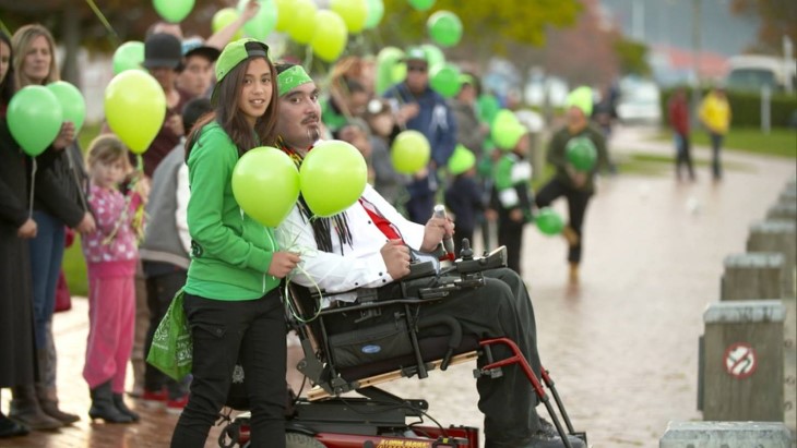 Raymond Ruru in his wheelchair with his young daughter Dyani, who is standing next to him. 